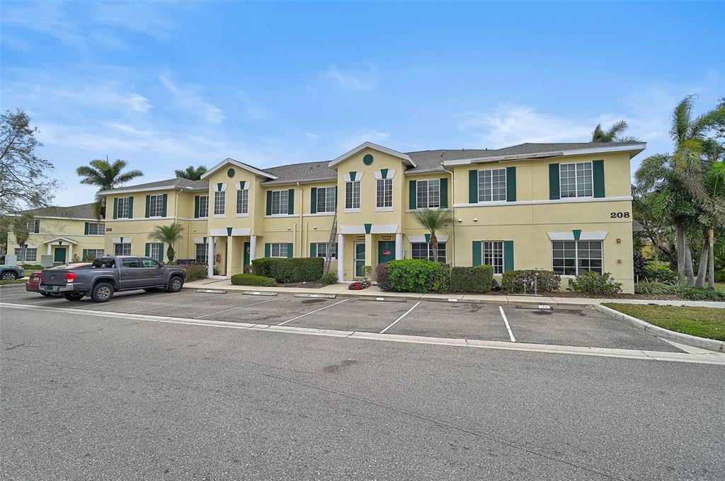 A two-story yellow apartment building with green shutters and a parking lot in front — 208 CAPE HARBOUR LOOP UNIT 108, BRADENTON, FL