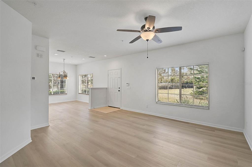 An open-concept living and dining area features light wood flooring, white walls, and ceiling fans — 208 CAPE HARBOUR LOOP UNIT 108, BRADENTON, FL