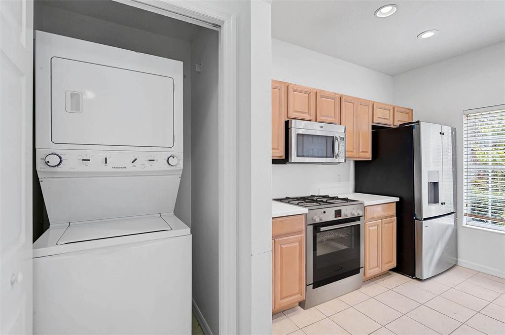 A kitchen features light wood cabinets, stainless steel appliances, and an adjacent stacked laundry unit — 208 CAPE HARBOUR LOOP UNIT 108, BRADENTON, FL