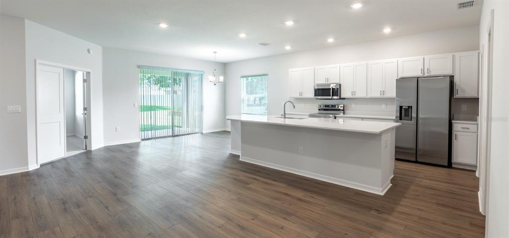 A living room with light wood floors, a beige sectional sofa, and an open kitchen — 1536 OTTER WOODS LANE, AUBURNDALE, FL