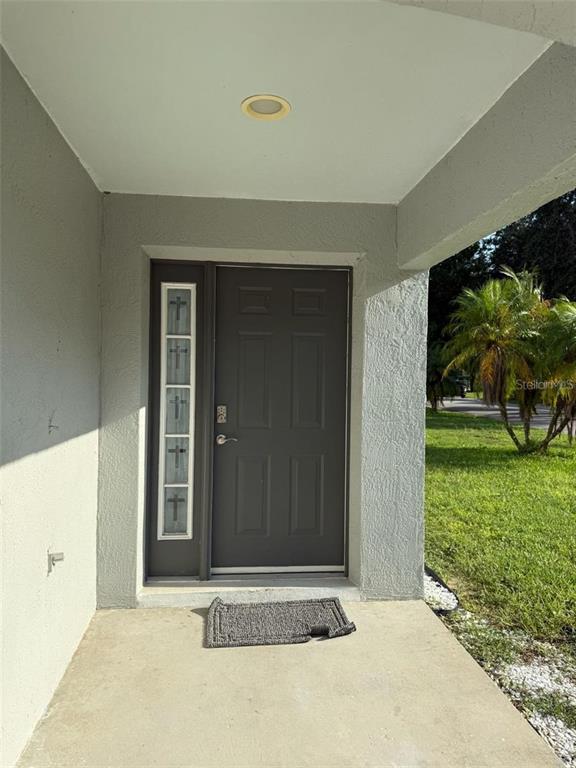 A gray front door with a vertical sidelight featuring cross-shaped glass inserts under a porch — 3059 BARBADOS LANE, HAINES CITY, FL