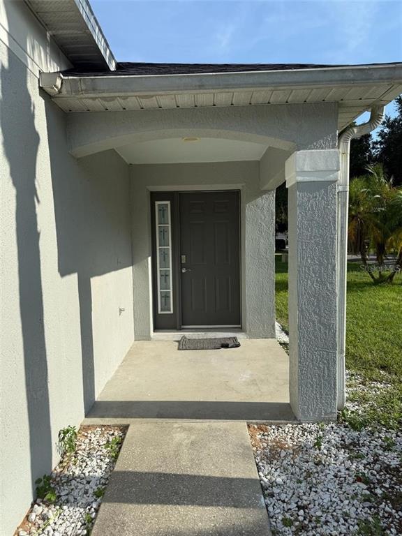 A covered concrete entryway leads to a dark gray front door with a side window panel — 3059 BARBADOS LANE, HAINES CITY, FL