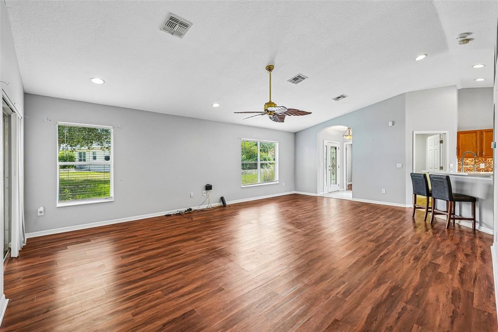 A spacious living room features wood-look flooring, light gray walls, a ceiling fan, and windows — 11455 INMAN COURT, SPRING HILL, FL