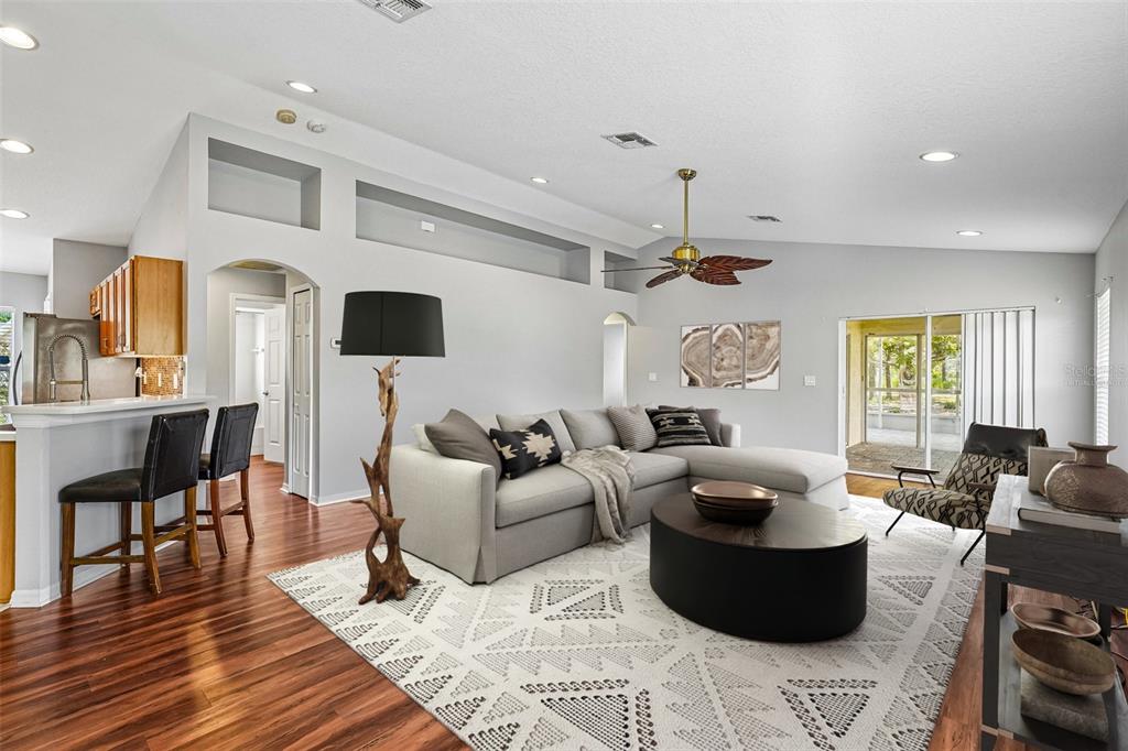 A living room with a sectional sofa, patterned area rug, and an open kitchen area — 11455 INMAN COURT, SPRING HILL, FL