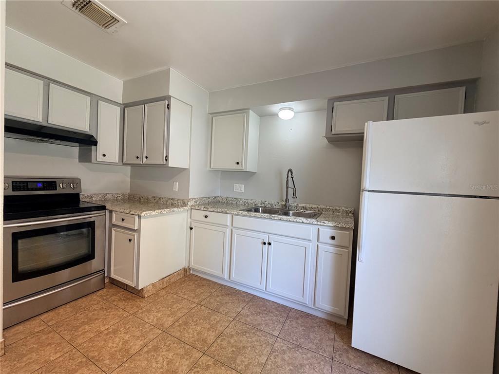A kitchen features white cabinets, granite countertops, stainless steel appliances, and tiled flooring — 84 E MARBRISA WAY, KISSIMMEE, FL