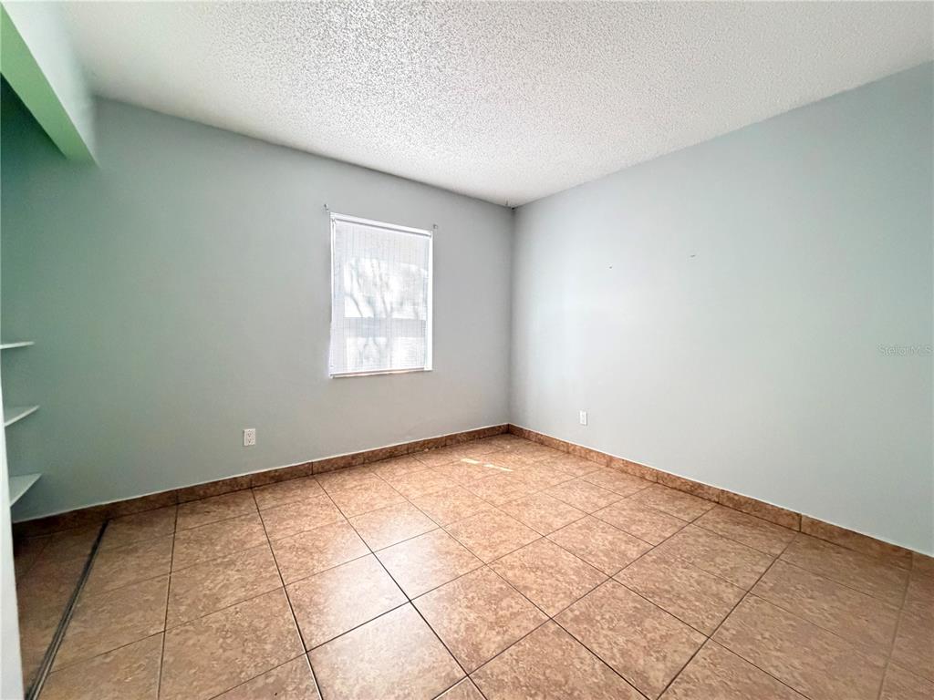 An empty room features light blue walls, tan tile flooring, and a single window — 84 E MARBRISA WAY, KISSIMMEE, FL