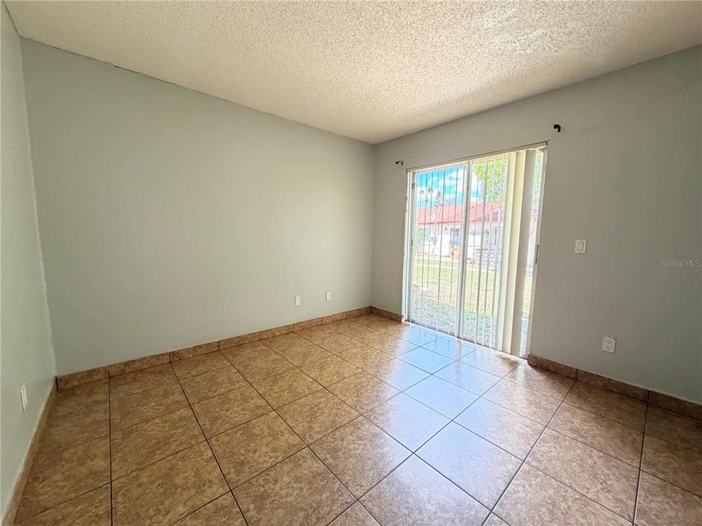 An empty room features light-colored walls, a textured ceiling, and brown square floor tiles — 84 E MARBRISA WAY, KISSIMMEE, FL