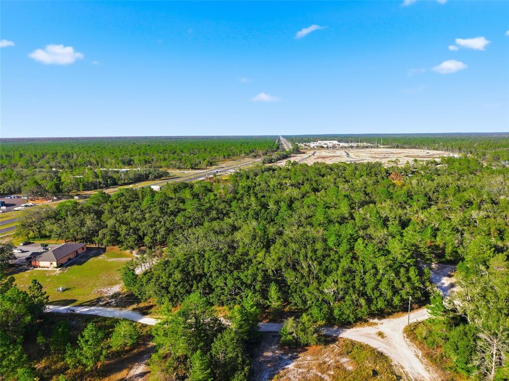 An aerial view shows a wooded lot with dirt roads and nearby commercial buildings — 11254 COMMERCIAL WAY, WEEKI WACHEE, FL
