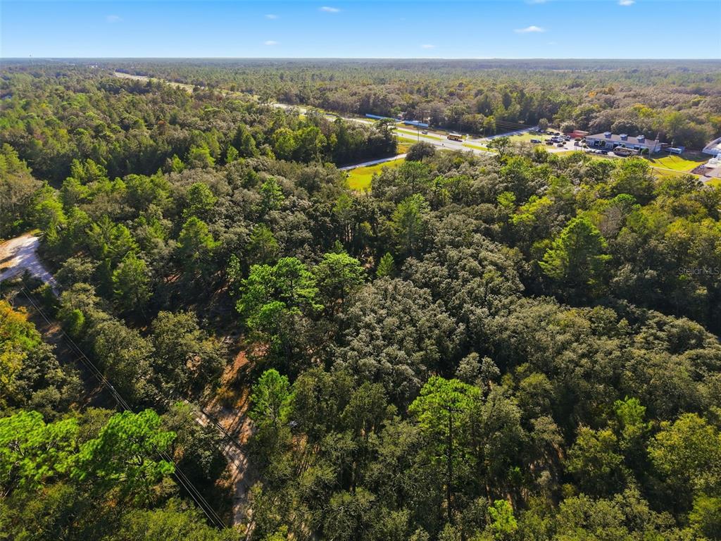 An aerial view shows a wooded lot adjacent to a highway with commercial buildings nearby — 11254 COMMERCIAL WAY, WEEKI WACHEE, FL