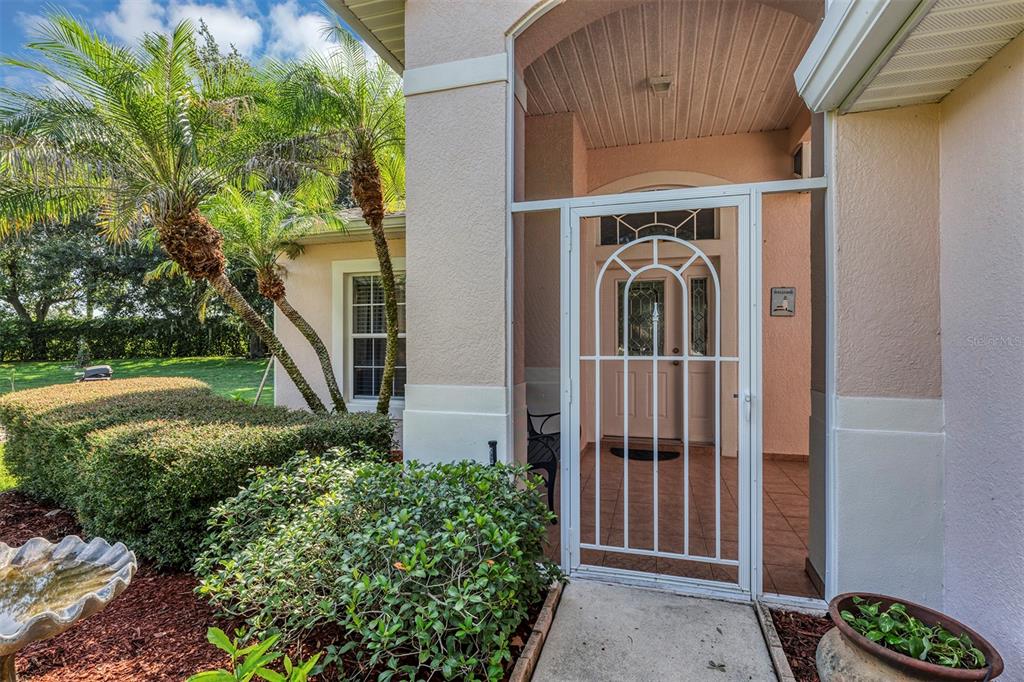 A white screen door leads to a tiled entryway with a front door and landscaping — 4958 PORTSMOUTH STREET, TAVARES, FL