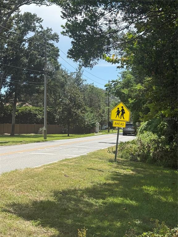 A yellow pedestrian crossing sign stands beside a paved road lined with trees and fences — PARK RIDGE GOTHA ROAD, WINDERMERE, FL