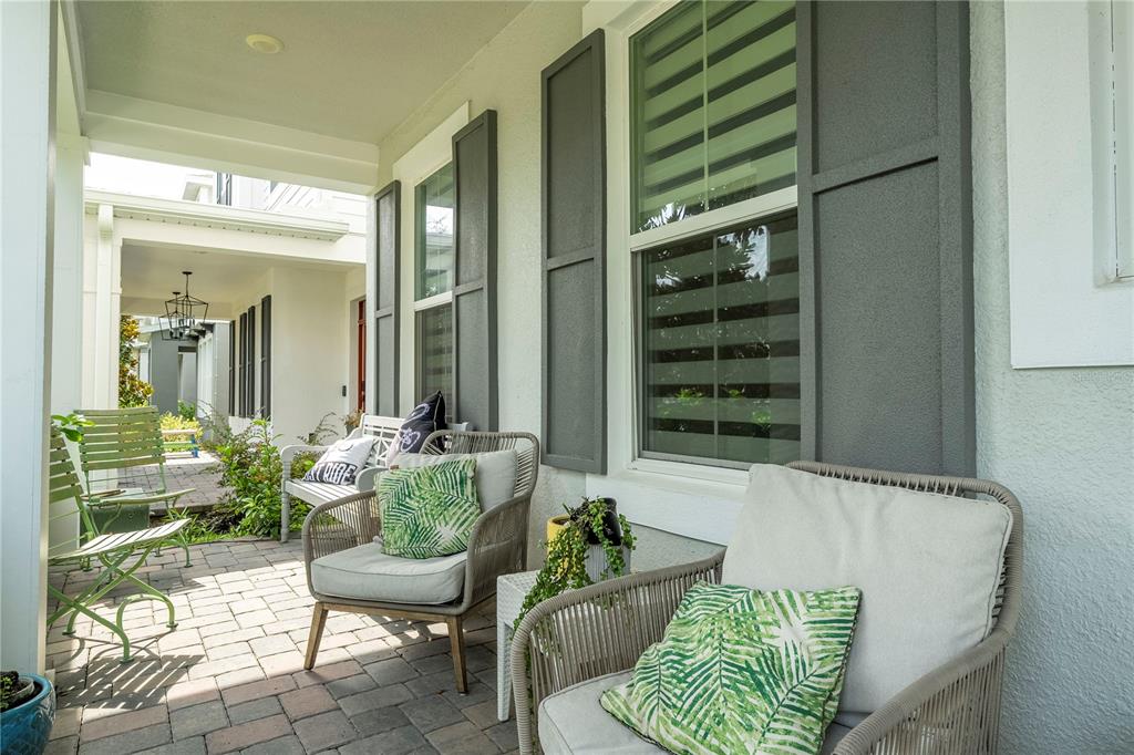 A covered patio features brick pavers, outdoor seating, and dark gray shutters on the exterior wall — 15068 LEBEAU LOOP, WINTER GARDEN, FL