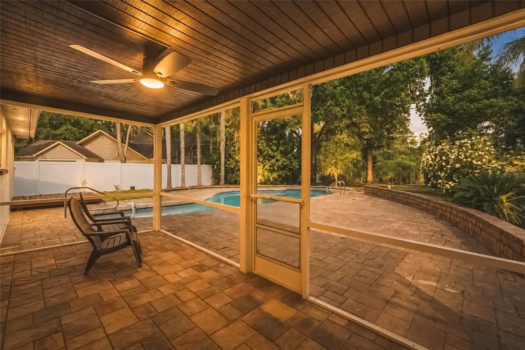 A screened-in patio with a ceiling fan overlooks a paved pool deck and backyard — 17002 PAULA LANE, LUTZ, FL