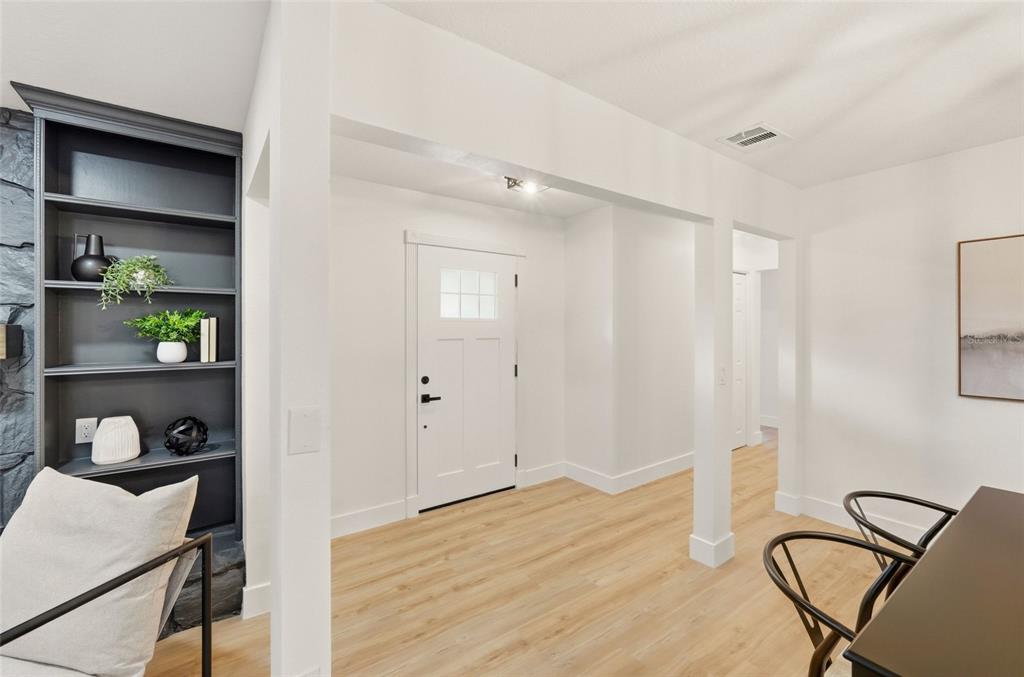 A bright entryway features light wood flooring, a white front door, and a dark bookshelf — 17002 PAULA LANE, LUTZ, FL