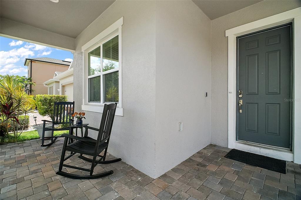 A covered front porch features a paver floor, two rocking chairs, and a dark gray door — 9153 CARMELA AVENUE, DAVENPORT, FL
