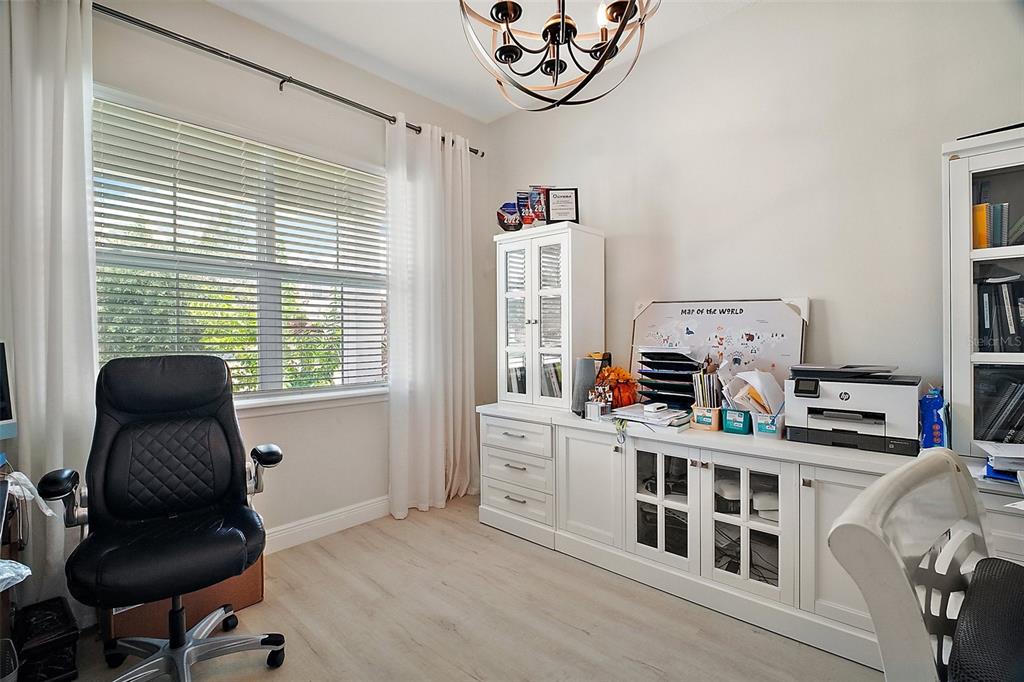A home office features a white desk, storage cabinets, a black chair, and a large window — 9153 CARMELA AVENUE, DAVENPORT, FL