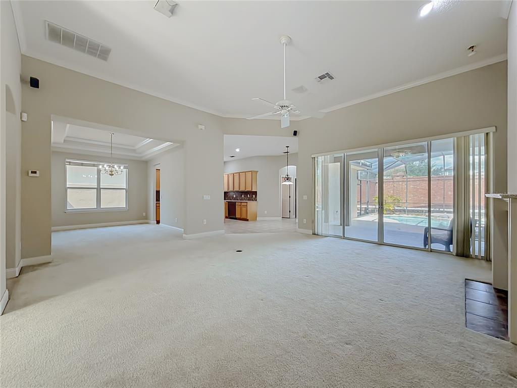 A spacious living room with beige carpeting, a ceiling fan, and sliding glass doors to a pool — 10824 WOODCHASE CIRCLE, ORLANDO, FL