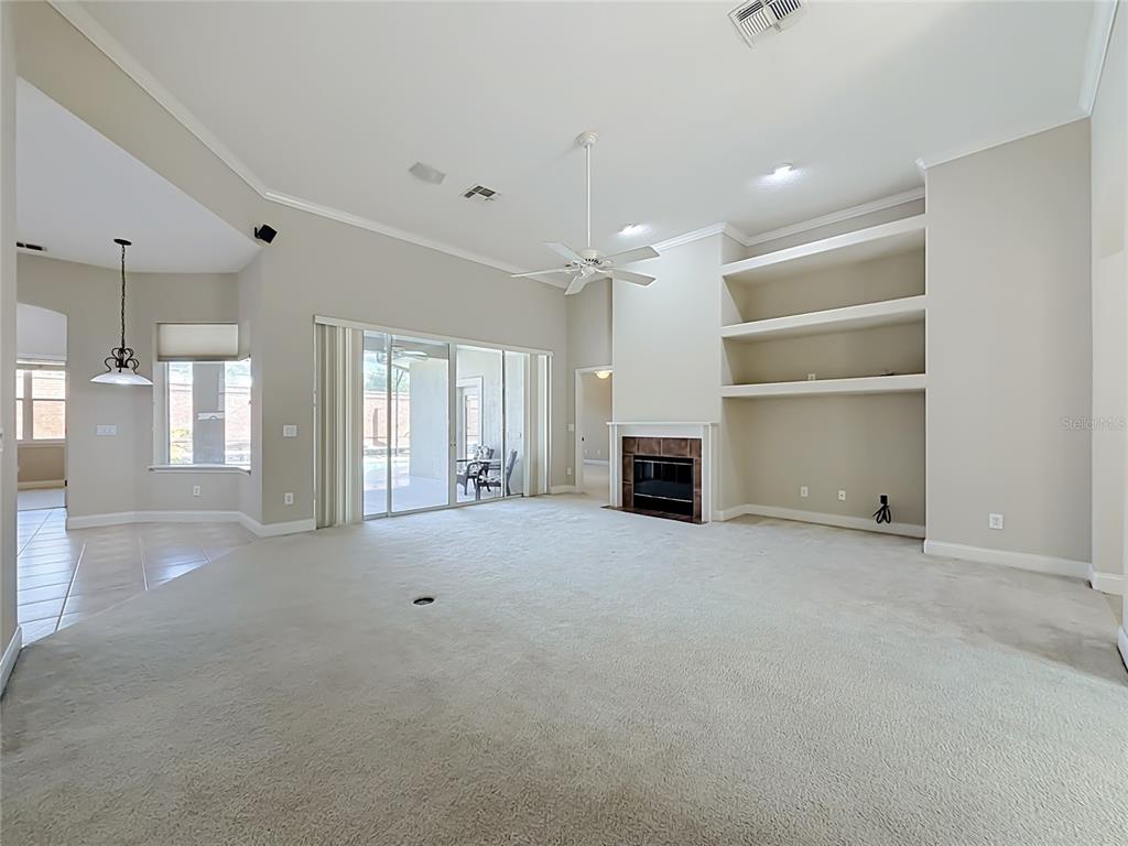 A spacious living room features beige carpeting, a fireplace, built-in shelves, and sliding glass doors — 10824 WOODCHASE CIRCLE, ORLANDO, FL