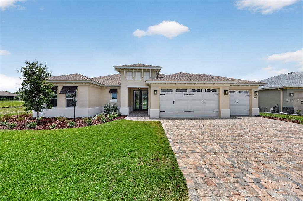 A single-story house with a beige stucco exterior, a paver driveway, and a three-car garage — 10706 SW 99TH PLACE, OCALA, FL