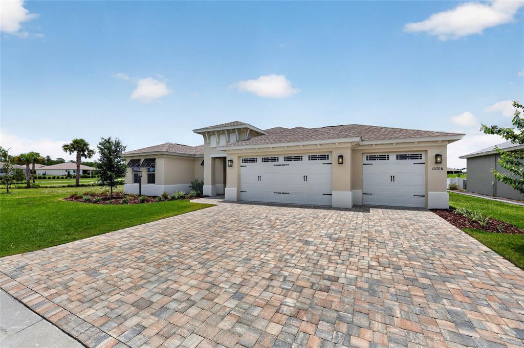 A single-story house with a paver driveway, three-car garage, and tan stucco exterior — 10706 SW 99TH PLACE, OCALA, FL