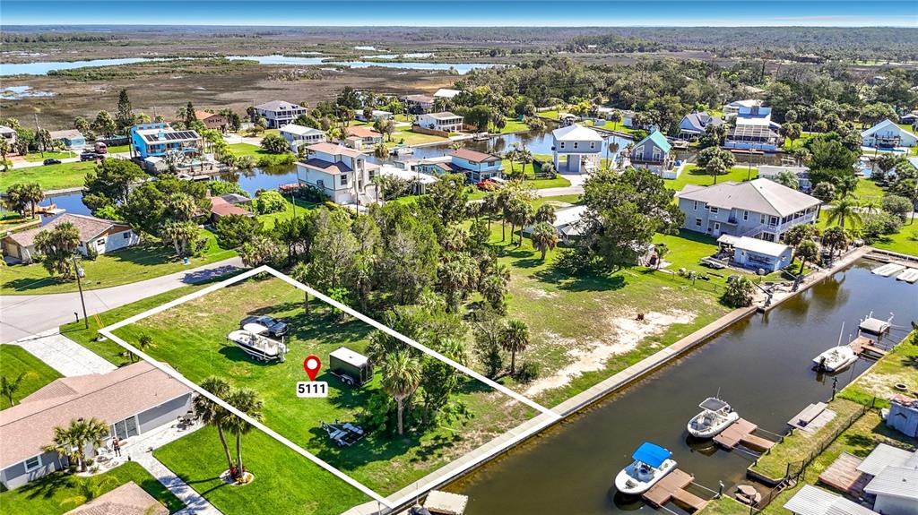 An aerial view shows a vacant waterfront lot with a boat and trailer parked on grass — 5099 CEDARBROOK LANE, HERNANDO BEACH, FL