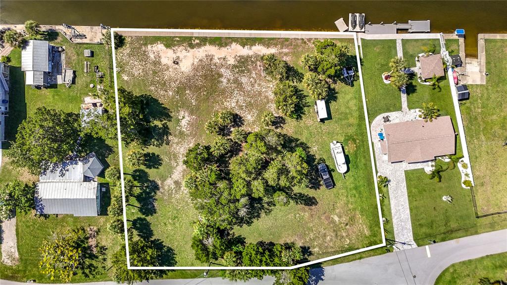 An aerial view shows a vacant, grassy residential lot bordered by water and neighboring homes — 5099 CEDARBROOK LANE, HERNANDO BEACH, FL