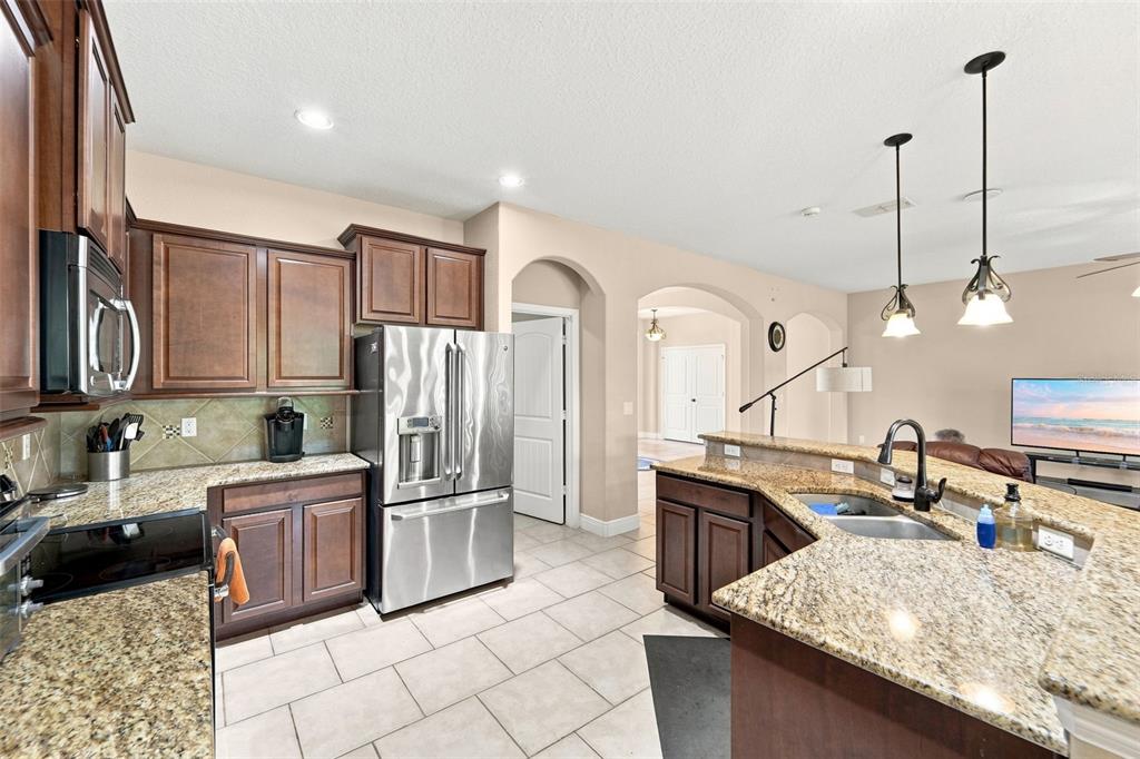 A kitchen features dark wood cabinets, granite countertops, stainless steel appliances, and tile flooring — 1451 DAYSTAR LANE, DELTONA, FL