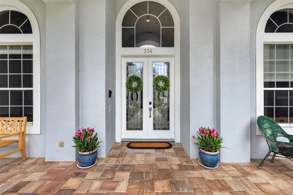 The front entrance features double glass doors, a stone patio, and two potted flower arrangements — 334 VISTA OAK DRIVE, LONGWOOD, FL