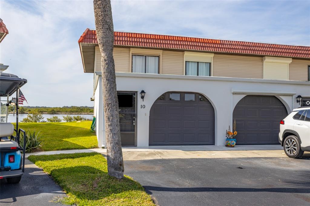 A two-story townhouse exterior features a white facade, arched garage doors, and a red roof — 10 OCEAN PALM VILLA N UNIT 10, FLAGLER BEACH, FL