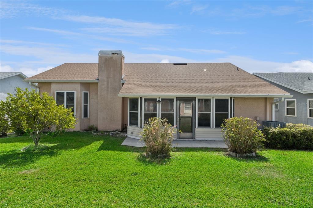 The rear exterior of a single-story house features a chimney, a sunroom, and a lawn — 6232 EGRET DRIVE, LAKELAND, FL