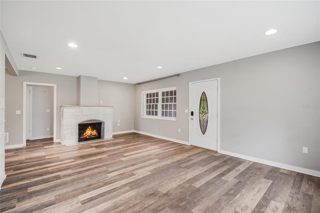 A living room features light gray walls, wood-look flooring, a white brick fireplace, and a door — 1635 GERTRUDE PLACE, MOUNT DORA, FL