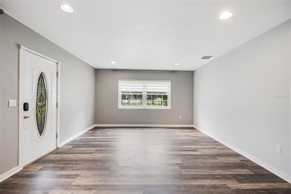An empty room features gray walls, wood-look flooring, recessed lighting, and a front entry door — 1635 GERTRUDE PLACE, MOUNT DORA, FL