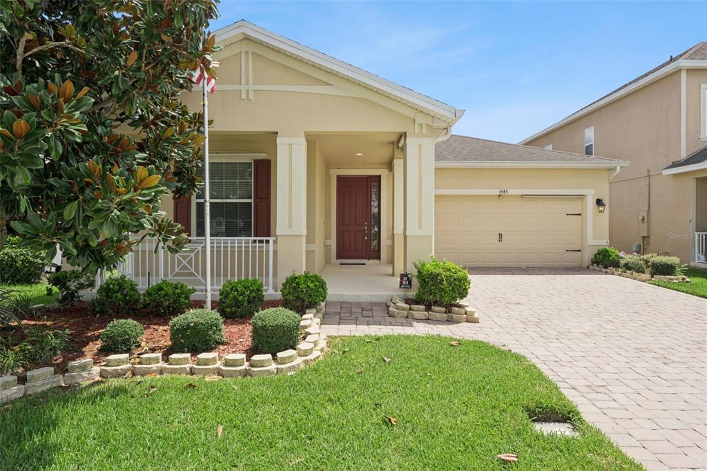 A single-story house with a beige stucco exterior, a two-car garage, and a front porch — 1543 CATERPILLAR STREET, ST CLOUD, FL