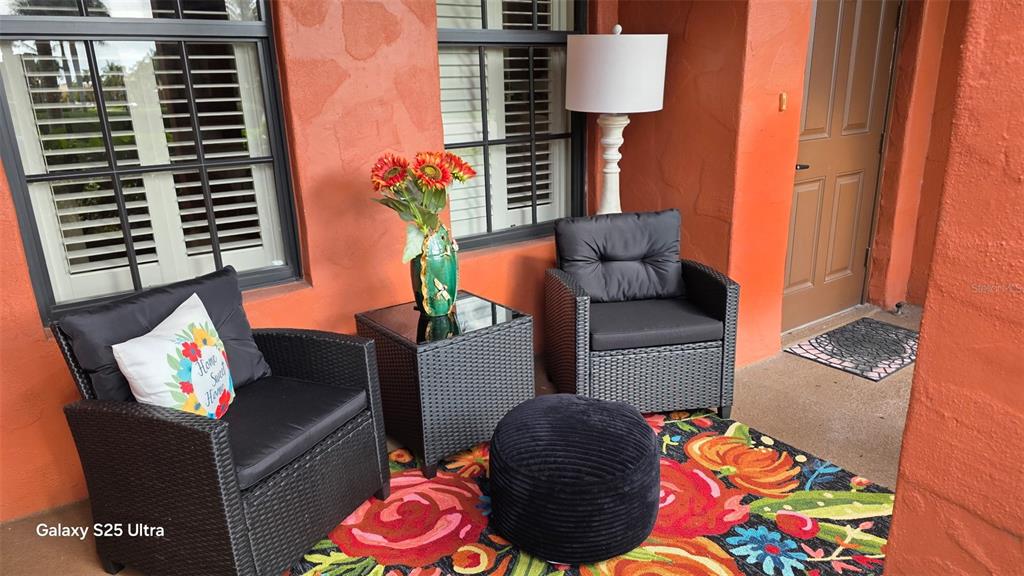 A covered patio features two black wicker chairs, a side table, and a colorful rug — 11220 PASEO GRANDE BOULEVARD UNIT 5204, FORT MYERS, FL