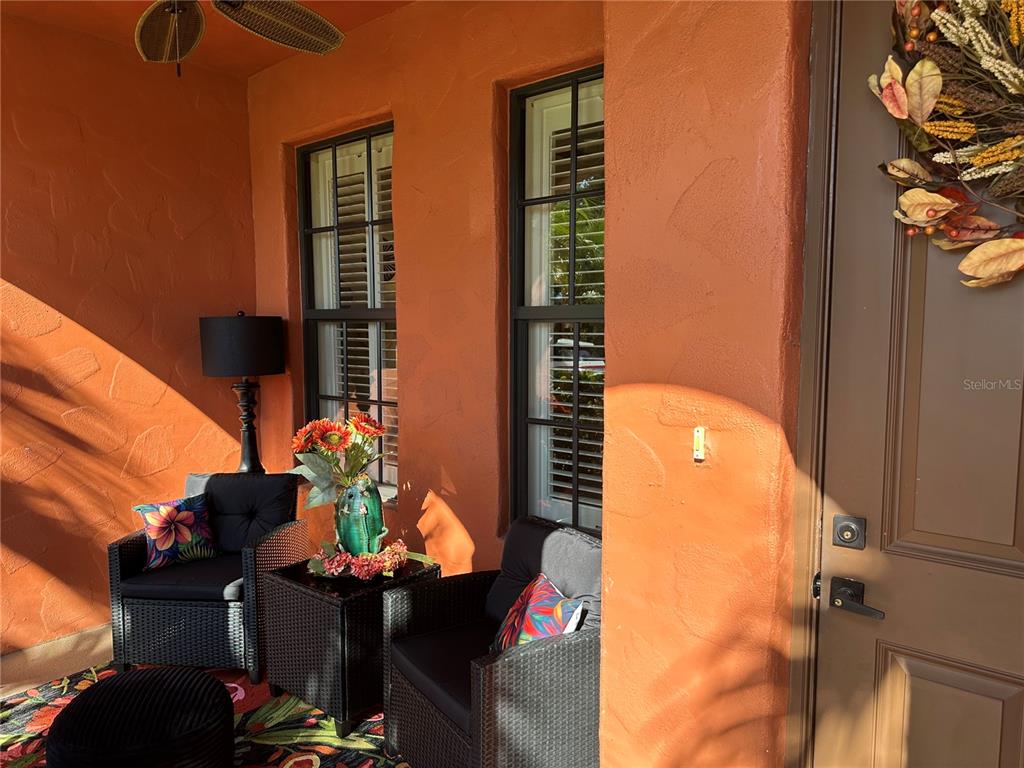 A covered porch features two wicker chairs, a small table, and orange stucco walls — 11220 PASEO GRANDE BOULEVARD UNIT 5204, FORT MYERS, FL