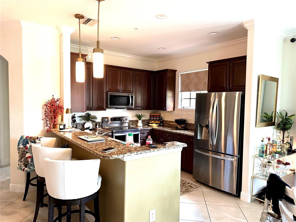 A kitchen features dark wood cabinets, granite countertops, stainless steel appliances, and a breakfast bar — 11220 PASEO GRANDE BOULEVARD UNIT 5204, FORT MYERS, FL
