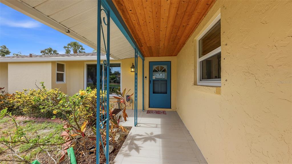 A covered porch with a blue door, wood-paneled ceiling, and yellow stucco exterior walls — 2220 DOUD STREET, SARASOTA, FL