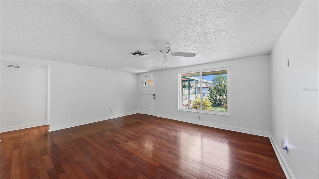 An empty living room features white walls, dark wood flooring, a ceiling fan, and a window — 2220 DOUD STREET, SARASOTA, FL