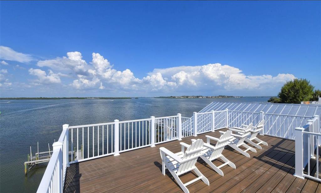 A wooden deck with white chairs overlooks a large body of water under a blue sky — 2516 AVENUE A, BRADENTON BEACH, FL