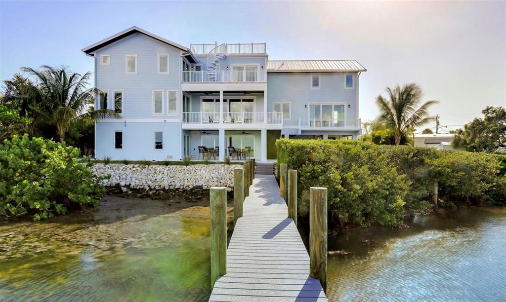A light blue multi-story house with a wooden dock extending into the water — 2516 AVENUE A, BRADENTON BEACH, FL