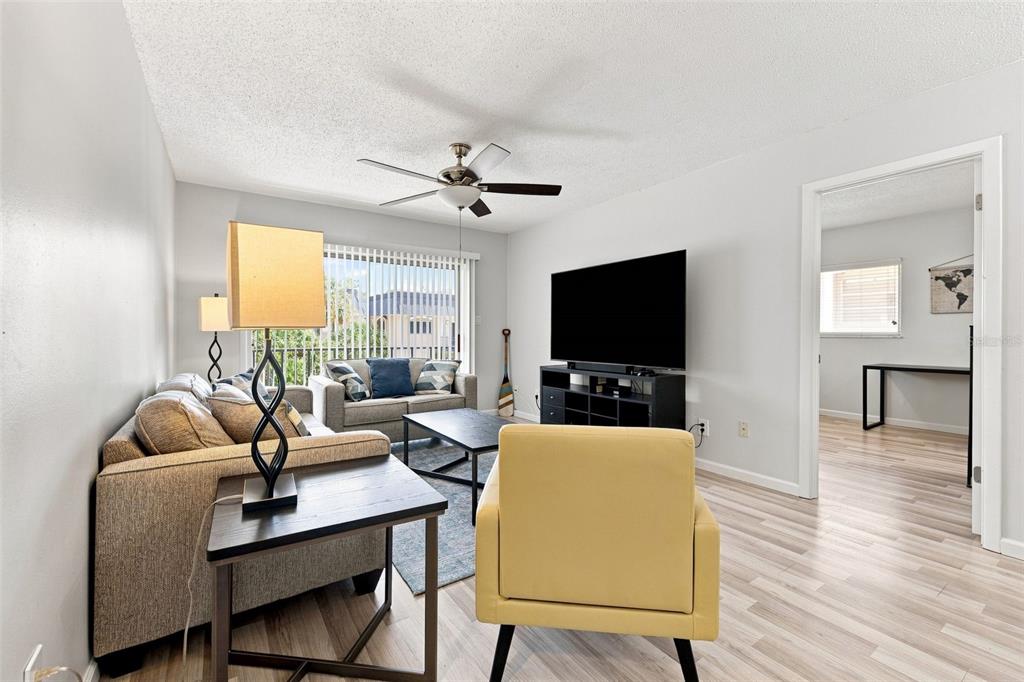 A living room features a sofa, yellow armchair, television on a stand, and wood flooring — 4606 W GRAY STREET UNIT 301, TAMPA, FL