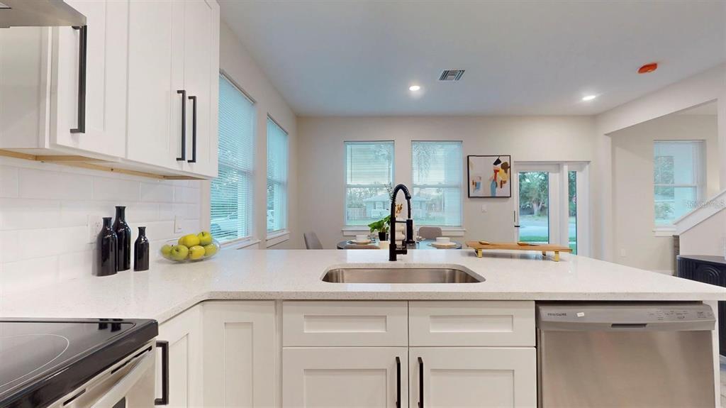 An open-concept kitchen and dining area features light wood flooring, white cabinetry, and modern lighting — 6910 DARTMOUTH AVENUE N, ST PETERSBURG, FL