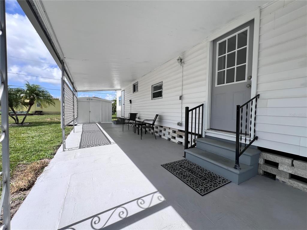 A covered porch features a gray door, stairs with black railings, and two outdoor chairs — 12674 SEMINOLE BOULEVARD UNIT C35, LARGO, FL