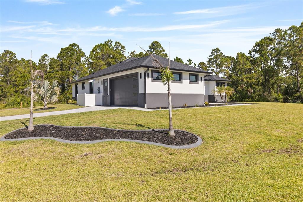 A modern, single-story house with a two-car garage sits on a grassy lot with trees — 2385 ECKER TERRACE, NORTH PORT, FL