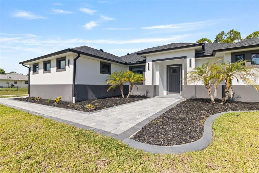 A modern, single-story house with white and gray exterior walls and a paved walkway — 2385 ECKER TERRACE, NORTH PORT, FL