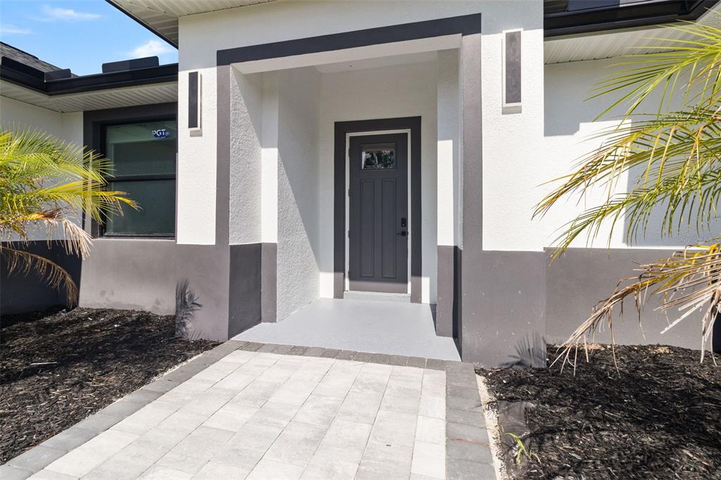 The exterior of a house features a gray front door, white walls, and stone pavers — 2385 ECKER TERRACE, NORTH PORT, FL