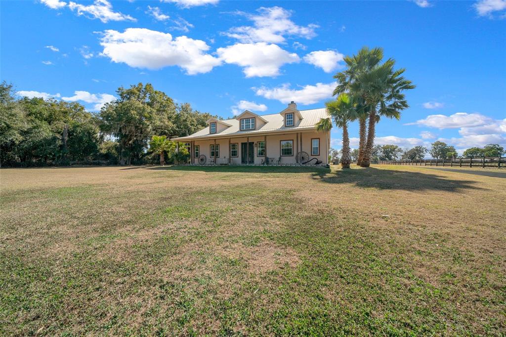 A tan farmhouse with a metal roof and dormer windows sits on a large grassy lot — 2198 W HIGHWAY 329, CITRA, FL