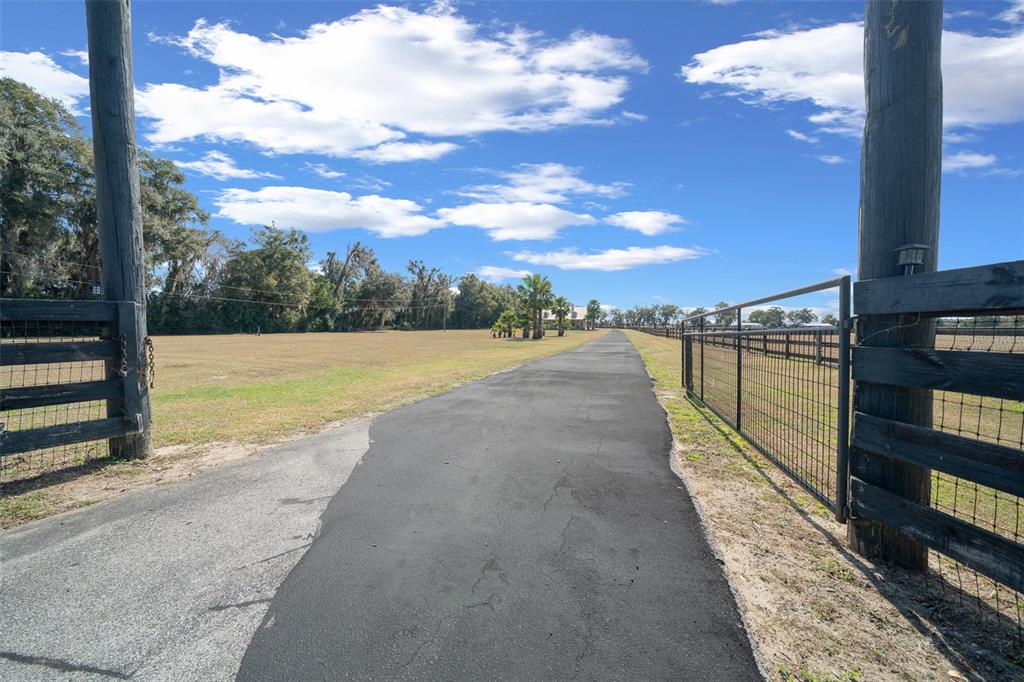 A paved driveway leads through an open gate toward a house in the distance — 2198 W HIGHWAY 329, CITRA, FL