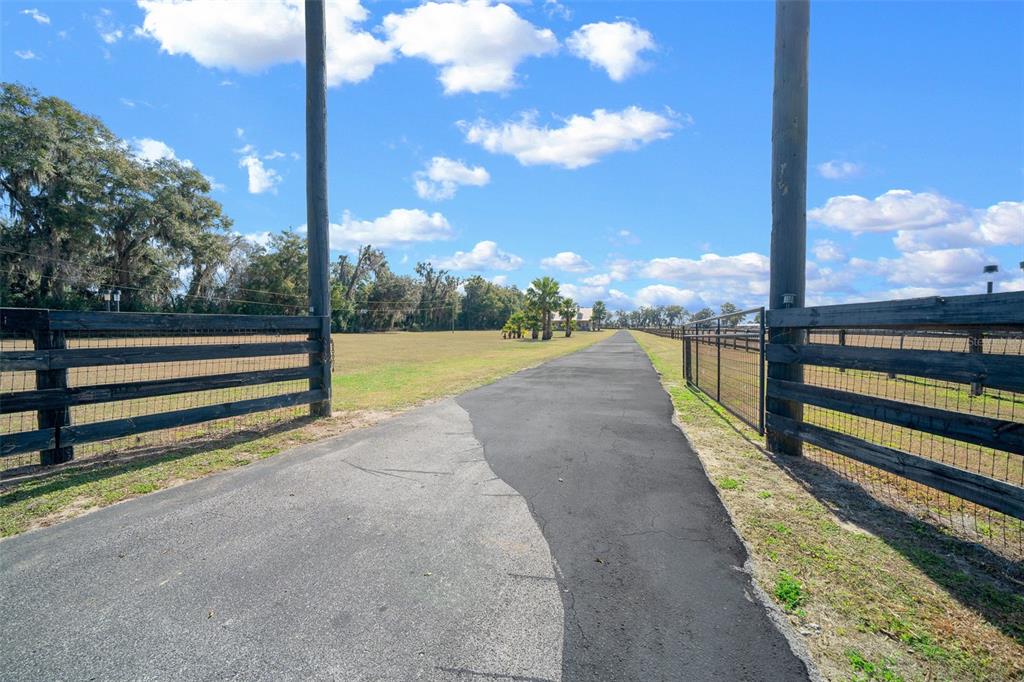 A paved driveway leads through a wooden fence gate toward a distant house and trees — 2198 W HIGHWAY 329, CITRA, FL
