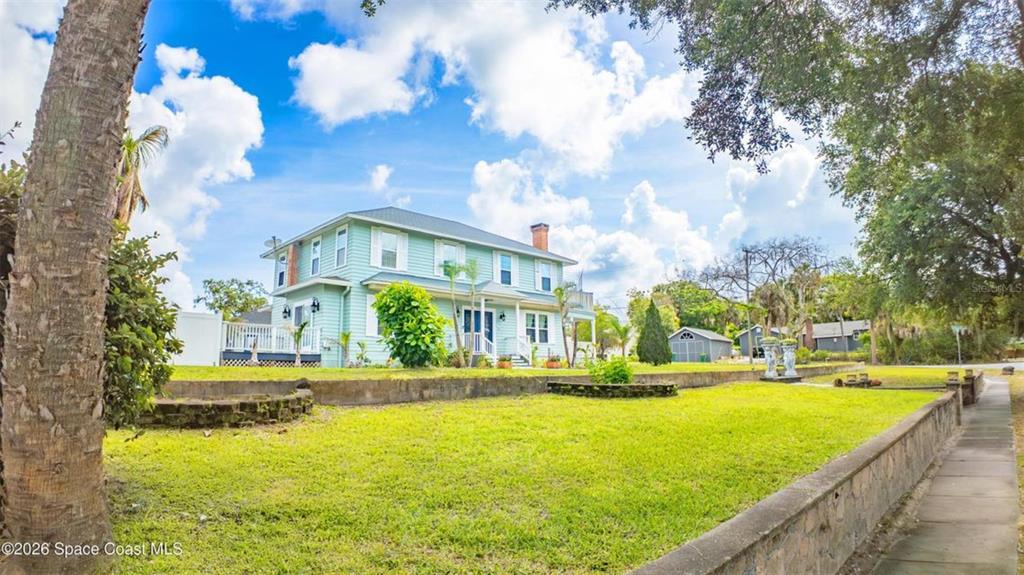 A light blue two-story house sits behind a low stone wall and grassy yard — 308 BELLAIR DRIVE, COCOA, FL